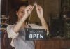 Opening A Restaurant In London? Here’s What You Need To Know A woman placing an 'Open' sign on the glass door of a restaurant