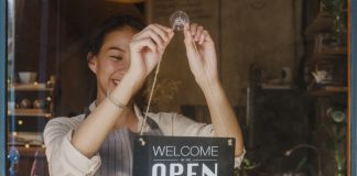 A woman placing an 'Open' sign on the glass door of a restaurant