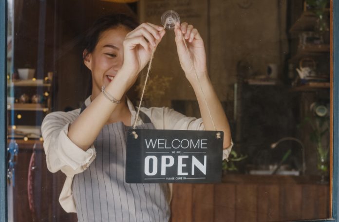 A woman placing an 'Open' sign on the glass door of a restaurant