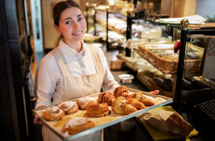 Woman holding a tray of baked food items in a bakery