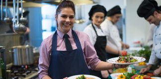 El entrenamiento del personal de tu restaurante para mejorar eficiencia: Una guía de 9 pasos Restaurant staff smiling and holding 2 plates in the kitchen