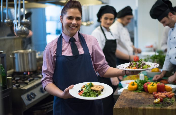 Restaurant staff smiling and holding 2 plates in the kitchen